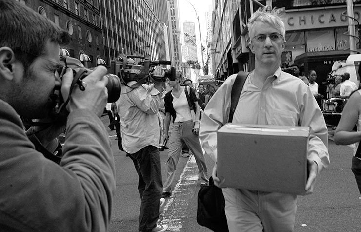 Man carrying a box through a crowd of photographers